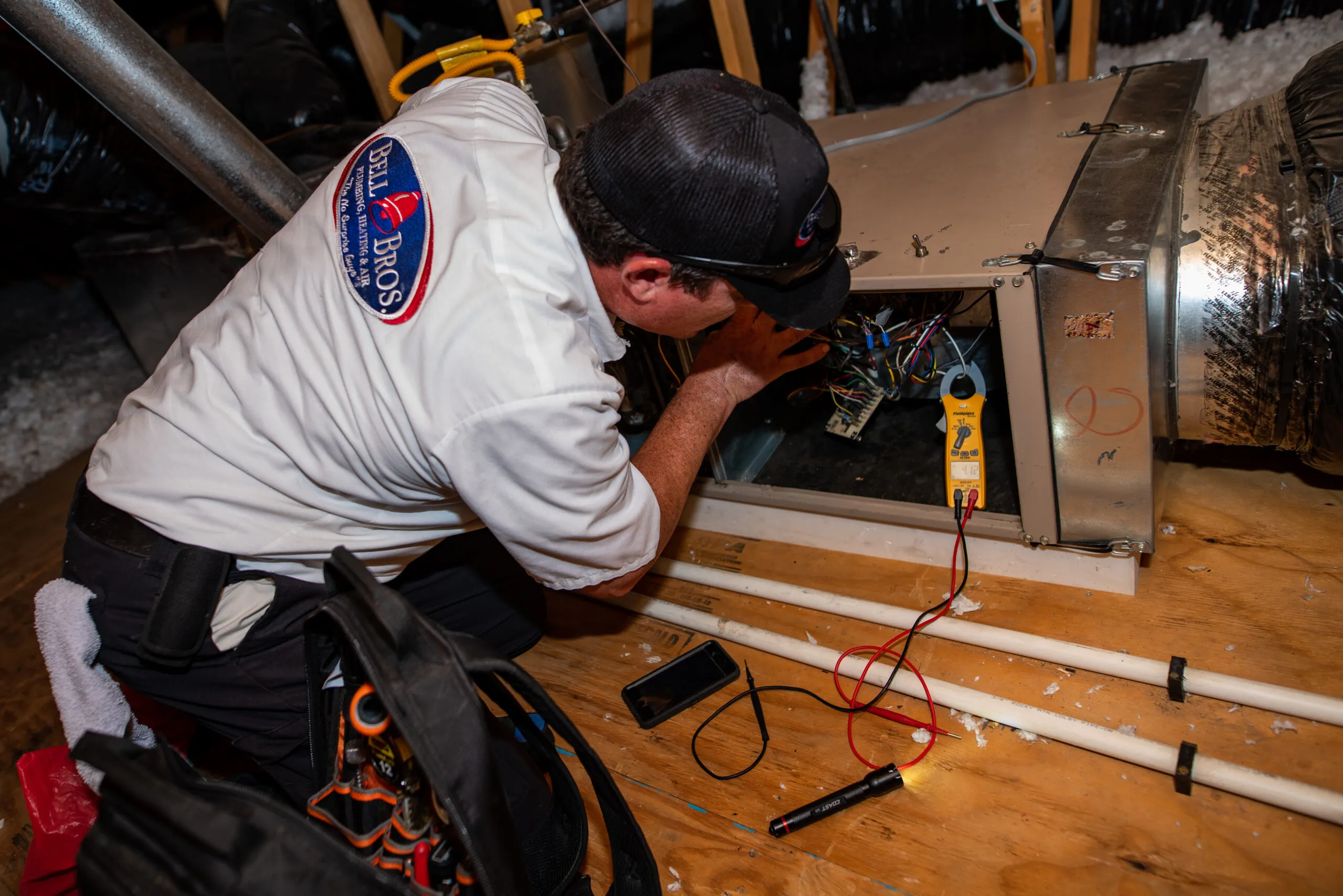 A technician from BellBrothersPlumbingHeatingandAir in Brea works on an HVAC system, inspecting electrical components inside an attic.